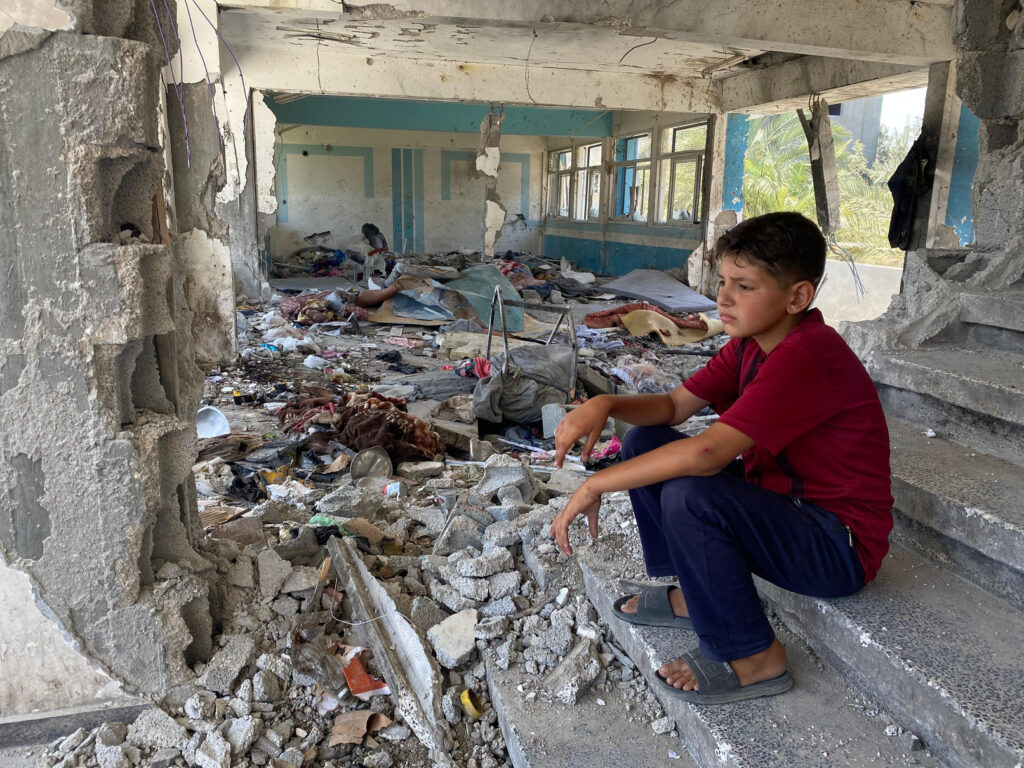 Menino sentado nos escombros de uma escola destruída da UNRWA em Nuseirat, Middle Areas. © 2024 UNRWA Foto