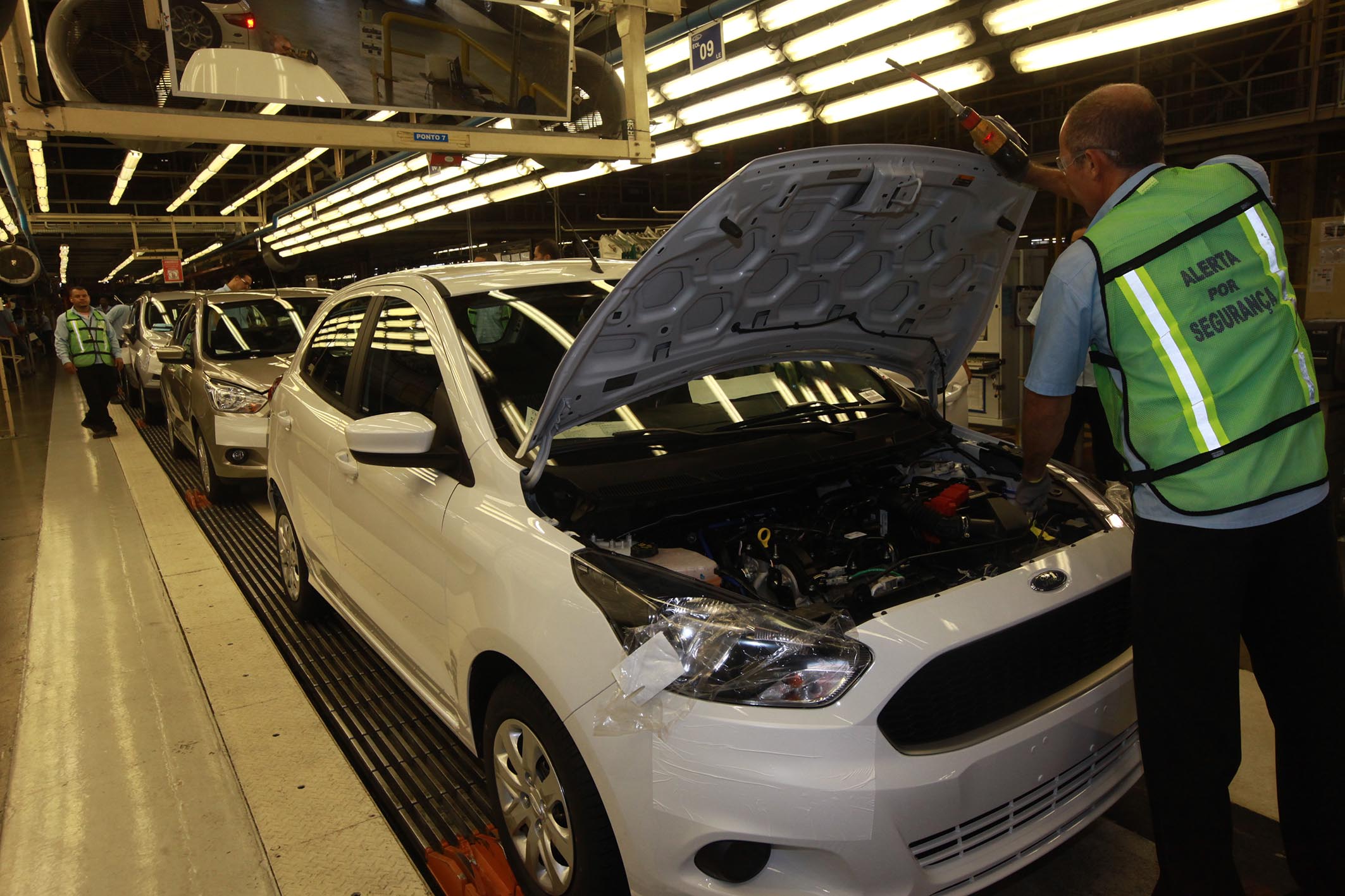 Operário inspeciona carro em linha de montagem automotiva
