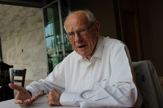 Homem idoso em conversa, gesticulando.
