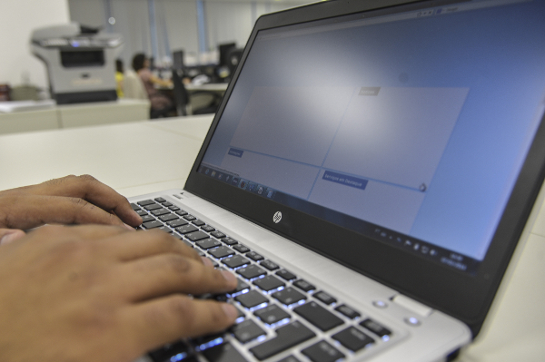 Mãos digitando em laptop HP em ambiente de escritório.