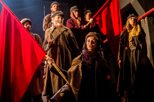 Mulheres e homens com bandeiras vermelhas em cena revolucionária.