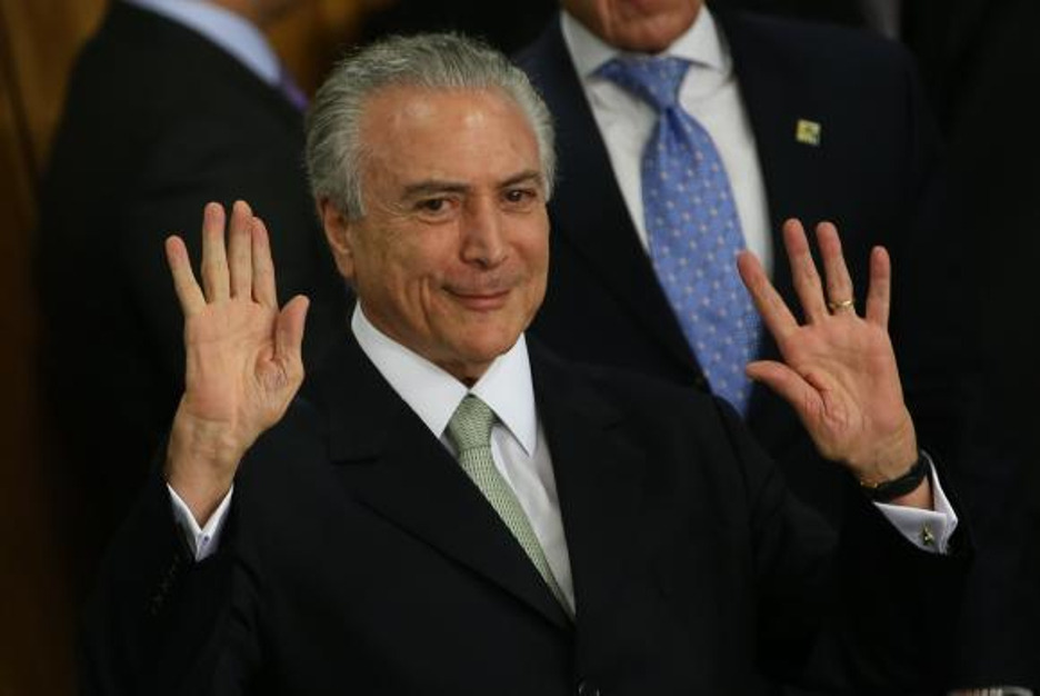 Michel Temer sorrindo, mãos levantadas em evento oficial