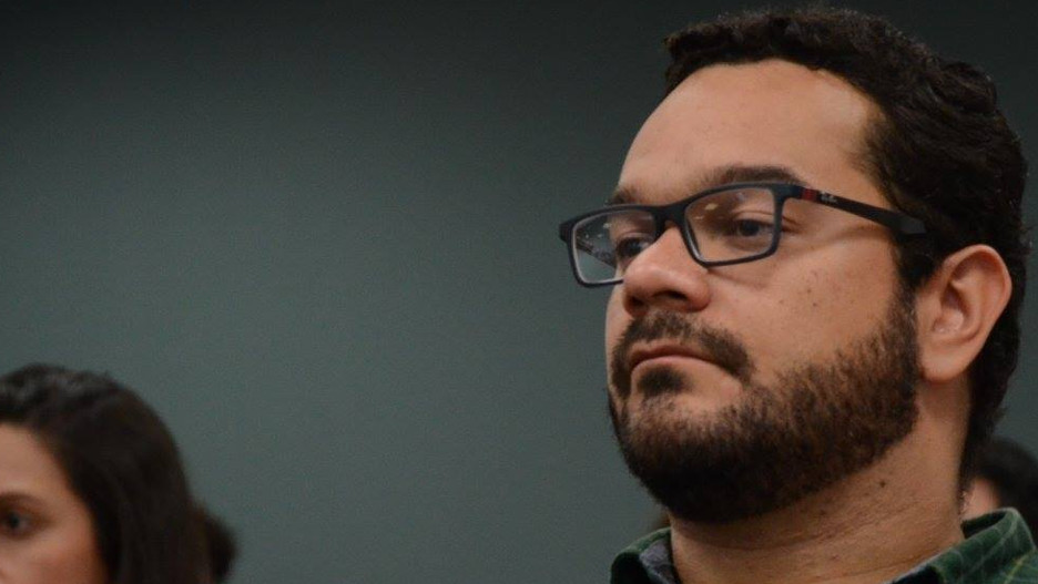 Homem barbudo de óculos em postura atenta e pensativa.