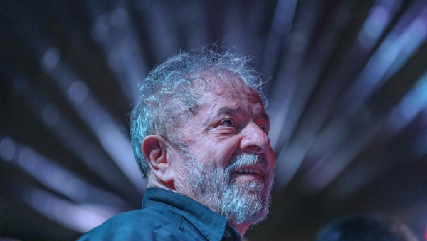Lula sorridente e reflexivo em palco iluminado