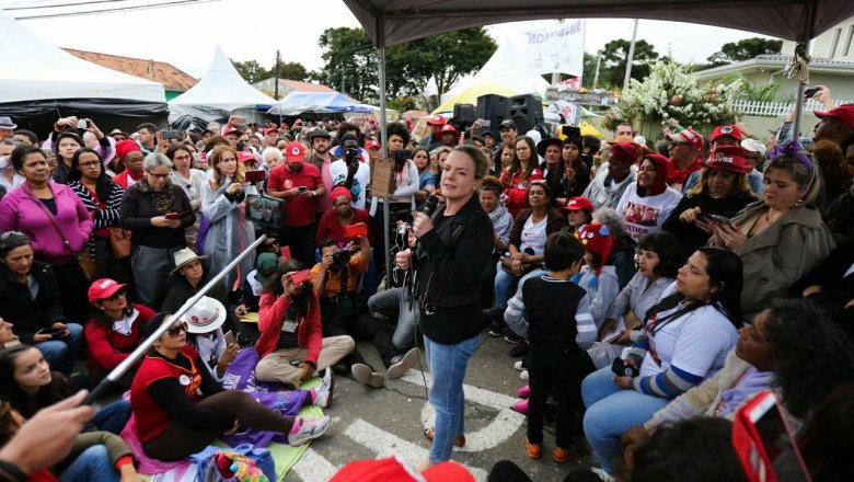 Mulher discursando em evento político com multidão engajada