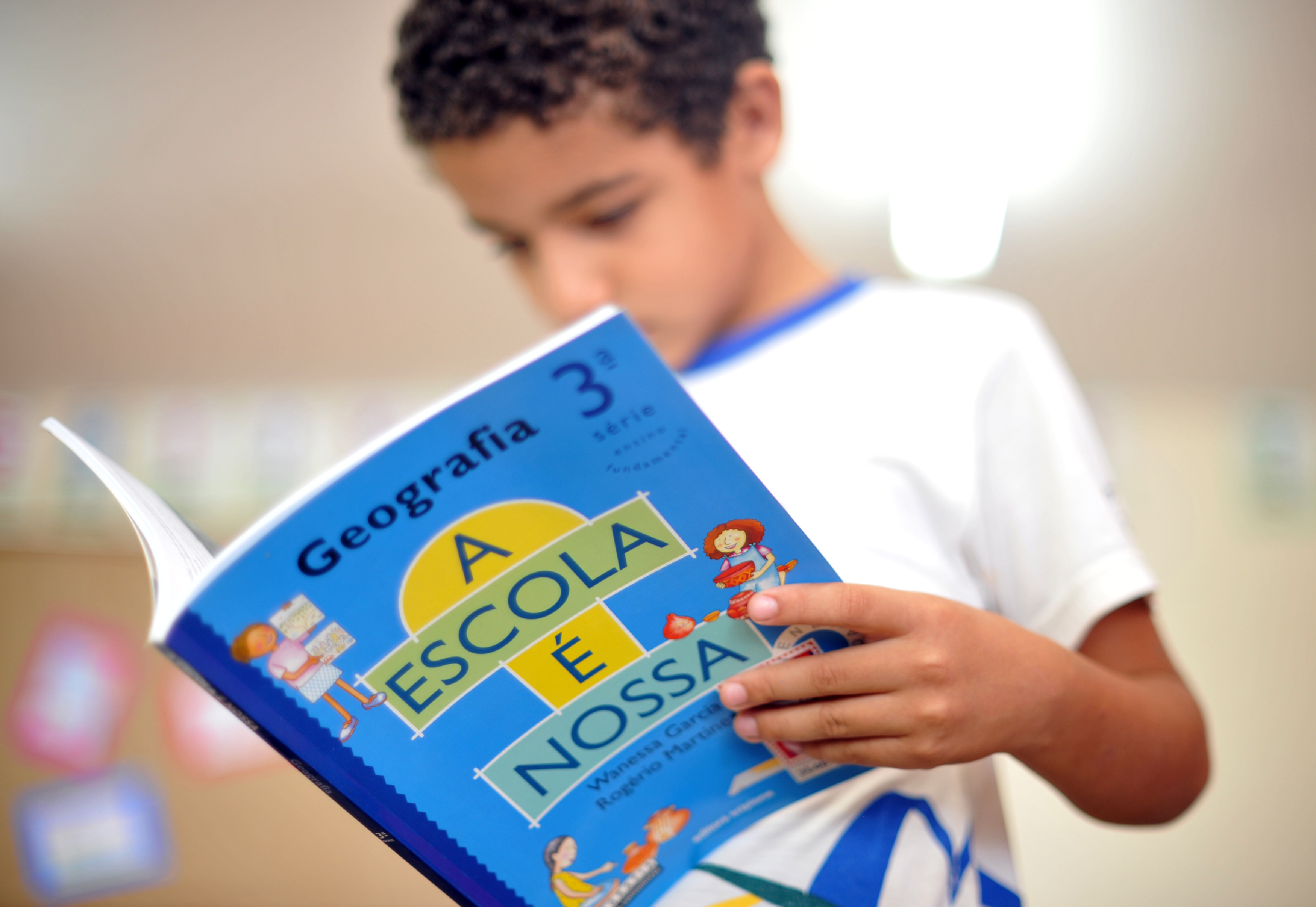 Criança estudando, livro de Geografia "A Escola É Nossa"