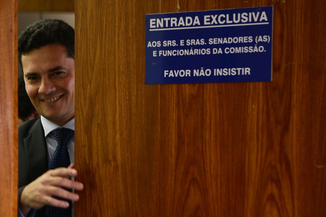 Sergio Moro sorri ao lado de placa de entrada exclusiva