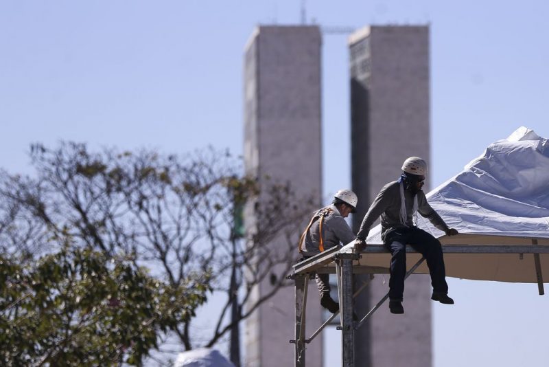 Trabalhadores montam estrutura, Congresso Nacional de Brasília ao fundo.