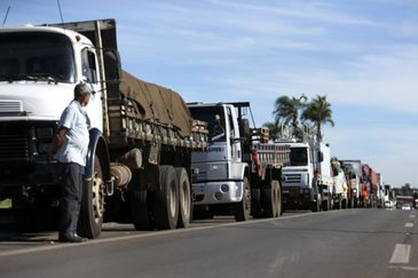 Longa fila de caminhões na estrada, com motorista pensativo