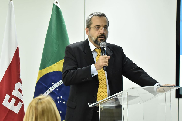 Palestrante em evento institucional com bandeiras do Brasil e ES