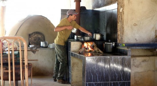 Homem cozinha em fogão a lenha tradicional no campo