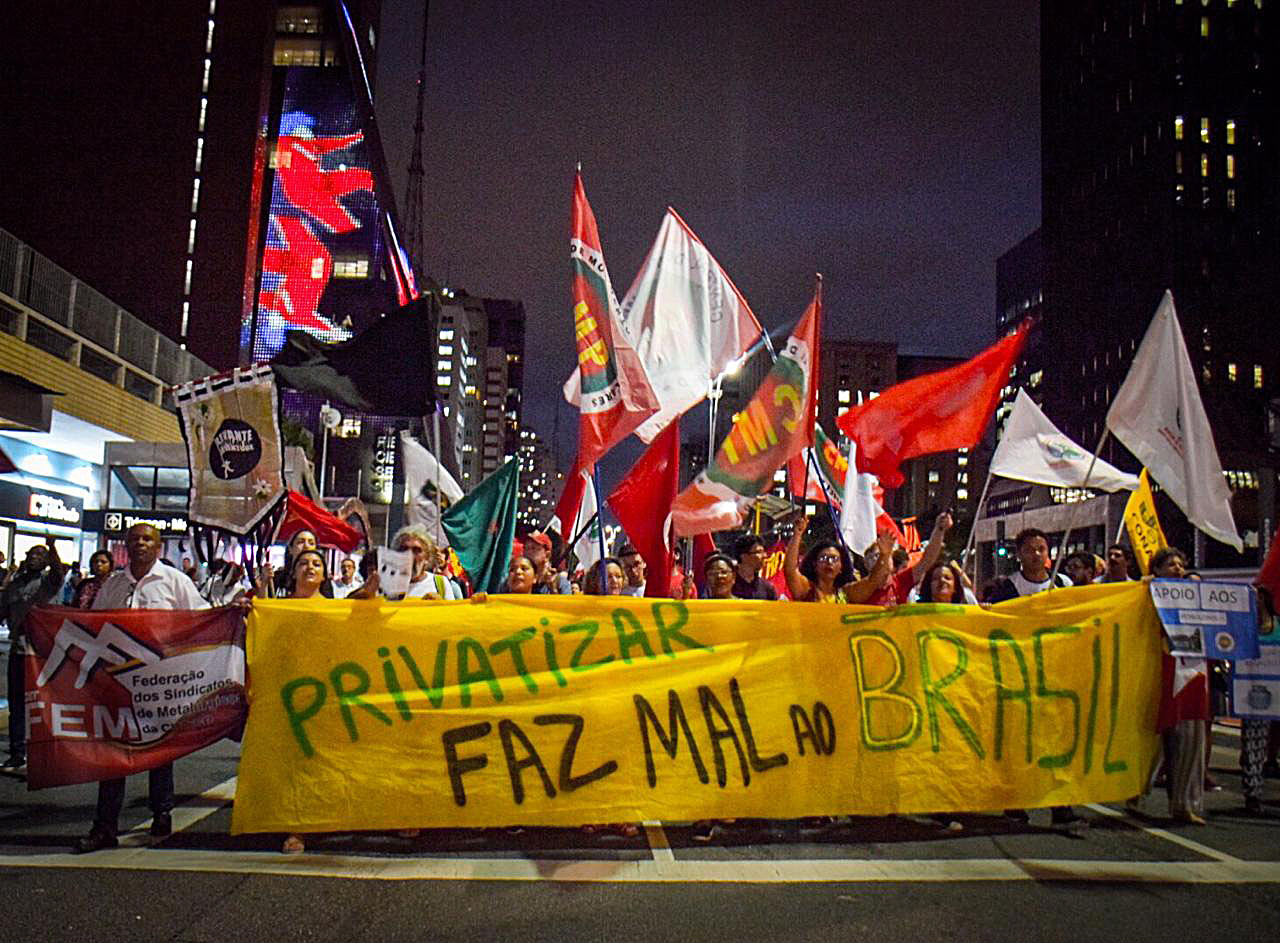 Protesto noturno contra privatização no Brasil com banners e bandeiras.