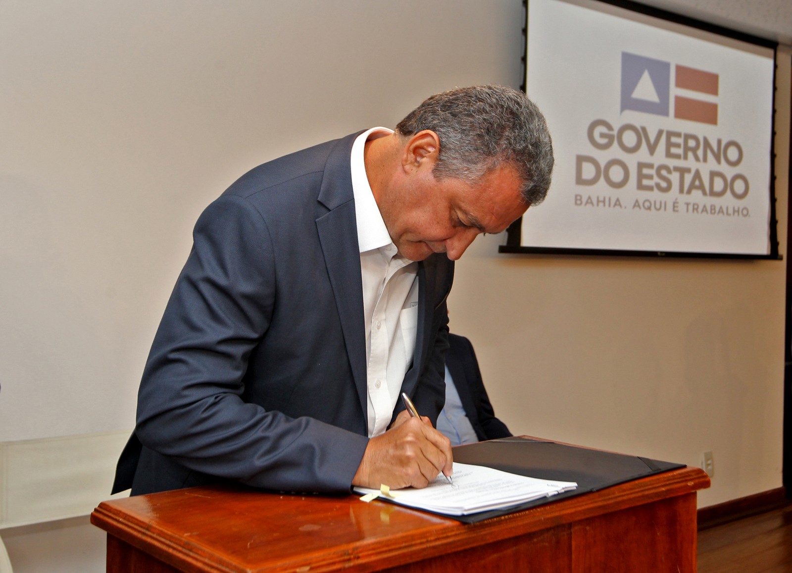 Homem assina documento oficial do Governo do Estado da Bahia.