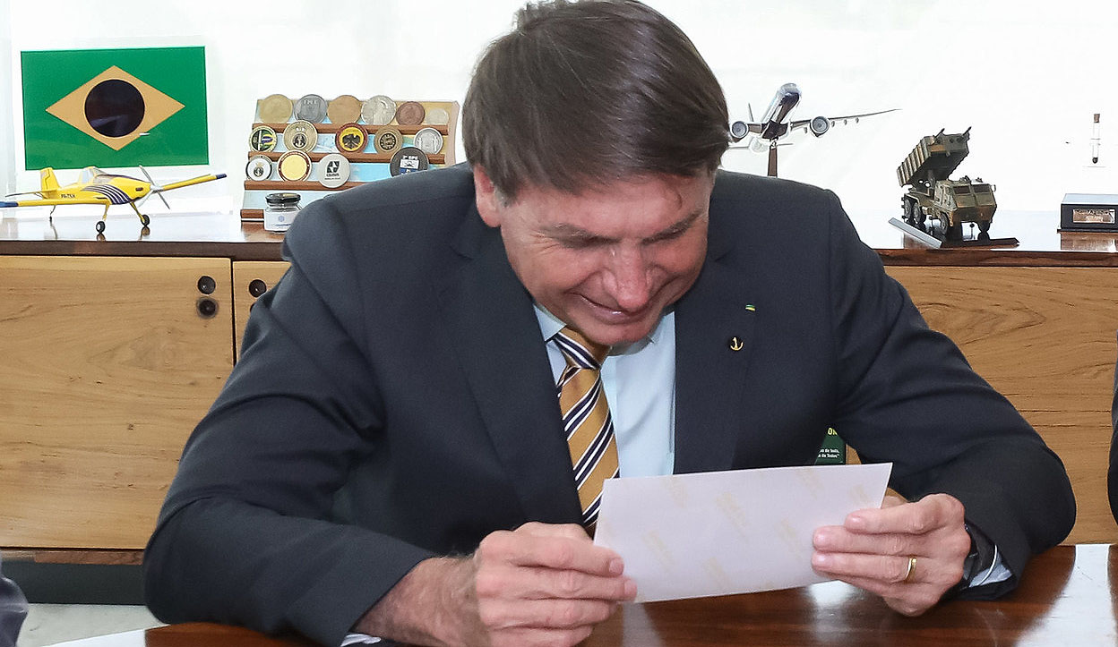 Bolsonaro lendo com símbolos militares e aeronáuticos