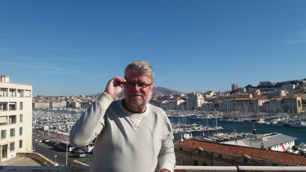 Homem sorridente em porto ensolarado de cidade mediterrânea