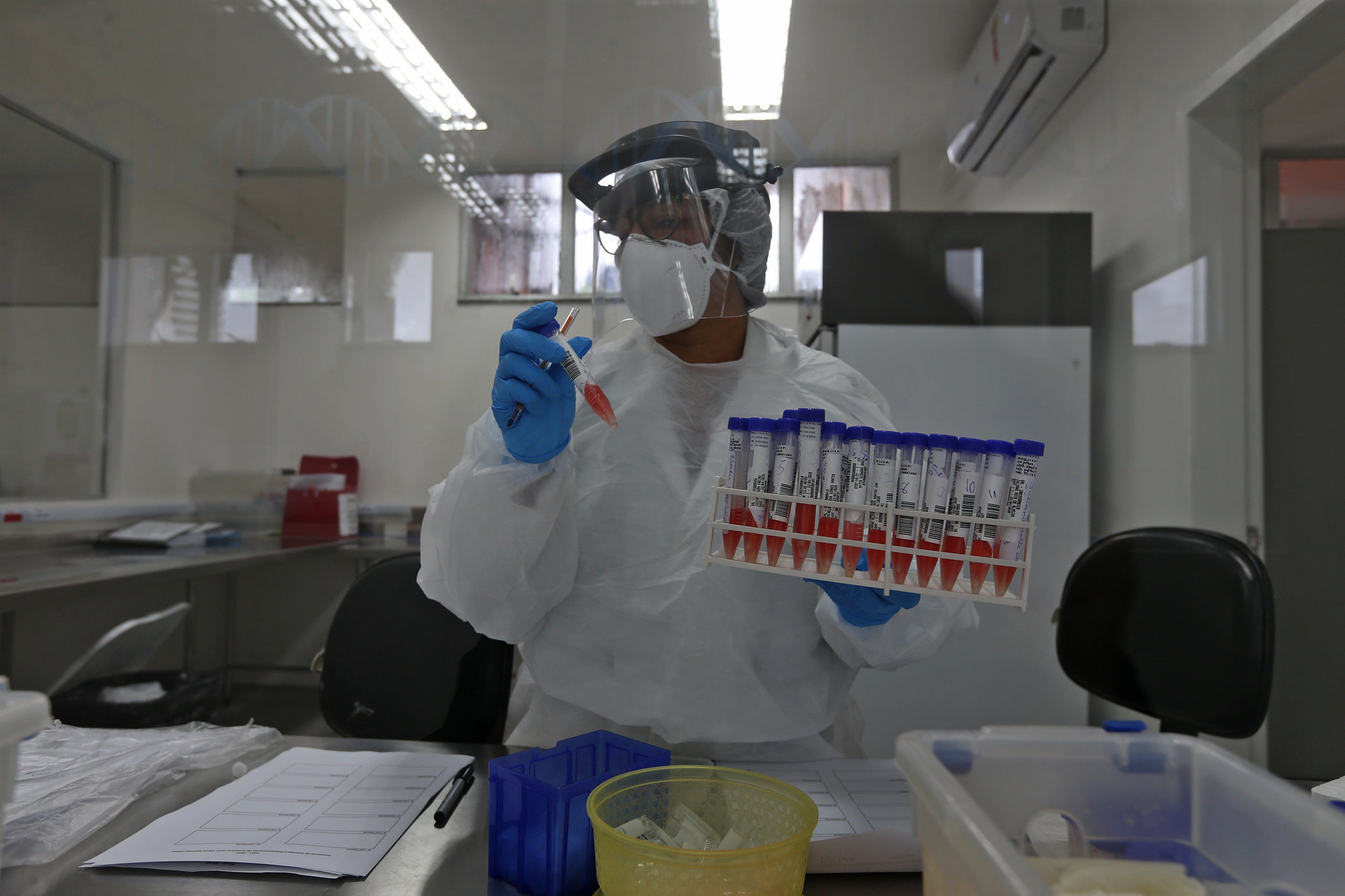Cientista em laboratório com EPI manuseia amostras de exames