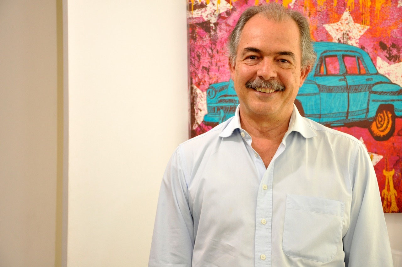 Homem sorridente com bigode e arte de carro clássico.