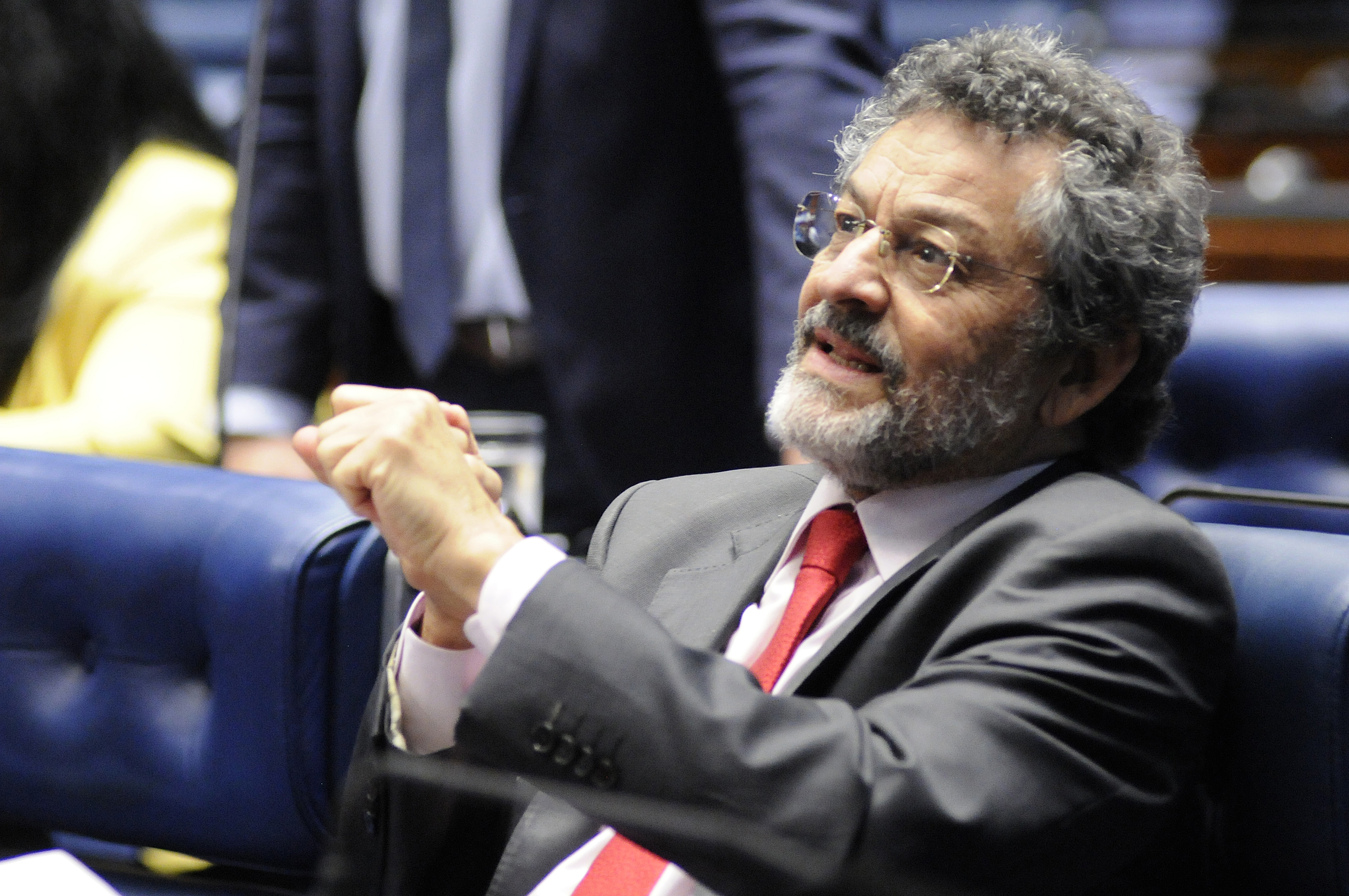 Homem em terno, gravata vermelha, atento em debate político