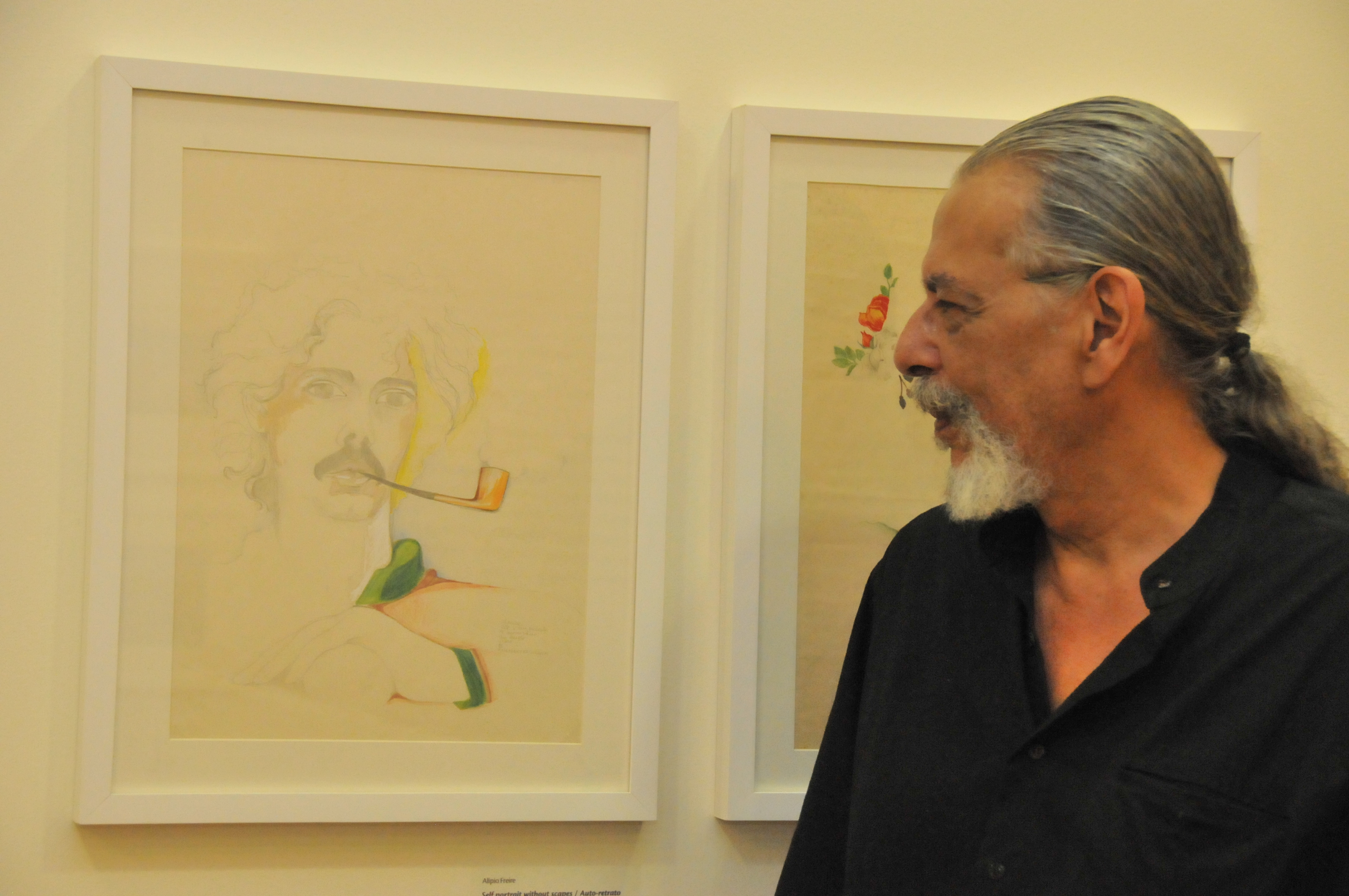 Alipio Freire observa auto-retrato em exposição de arte.