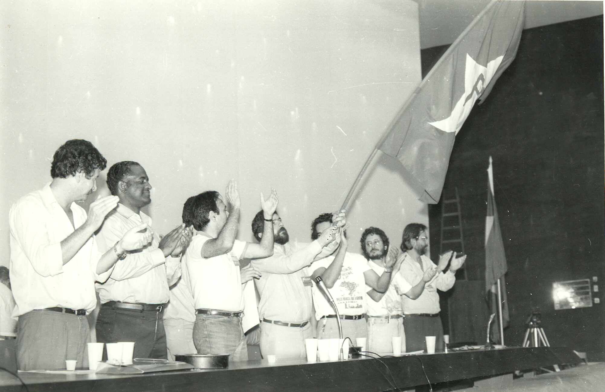 Lideranças em evento político com bandeira e aplausos.