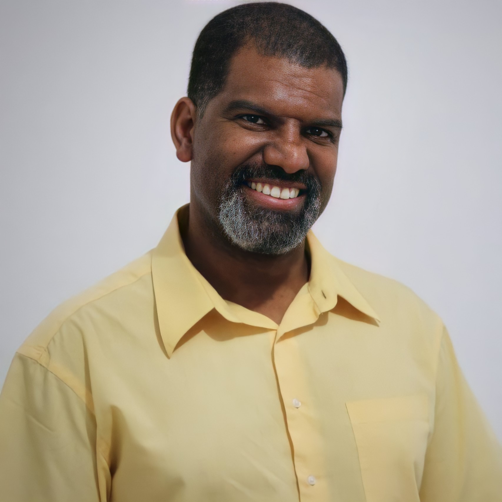 Homem sorridente com barba grisalha e camisa amarela