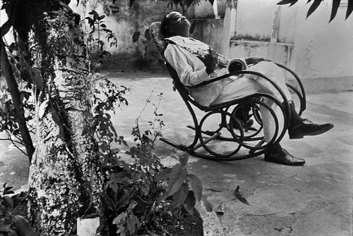 Pessoa idosa relaxando em cadeira de balanço em pátio.