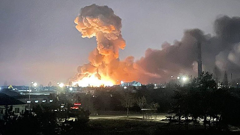Explosão massiva e incêndio industrial à noite.