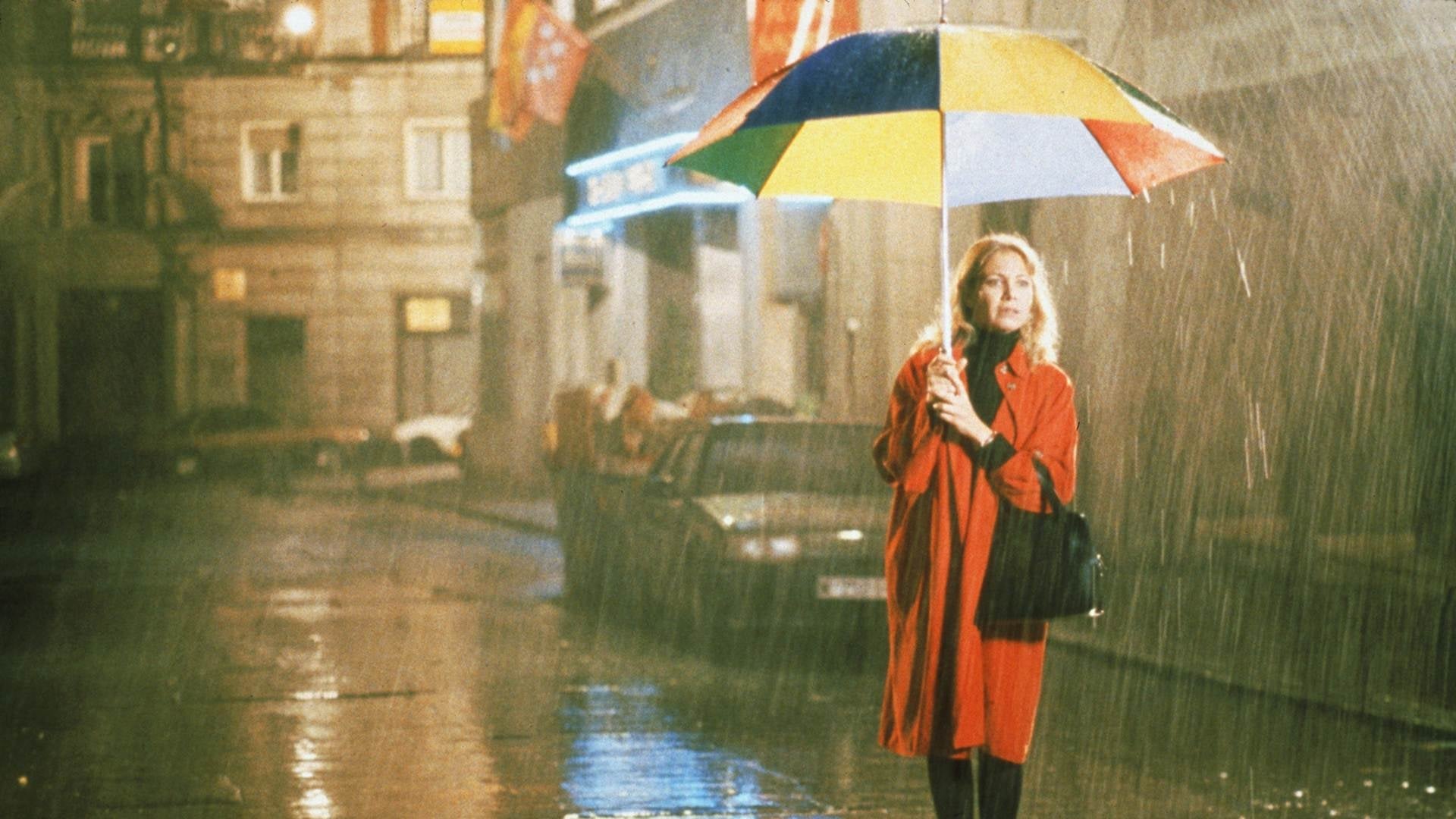 Mulher com guarda-chuva colorido na chuva em rua noturna.
