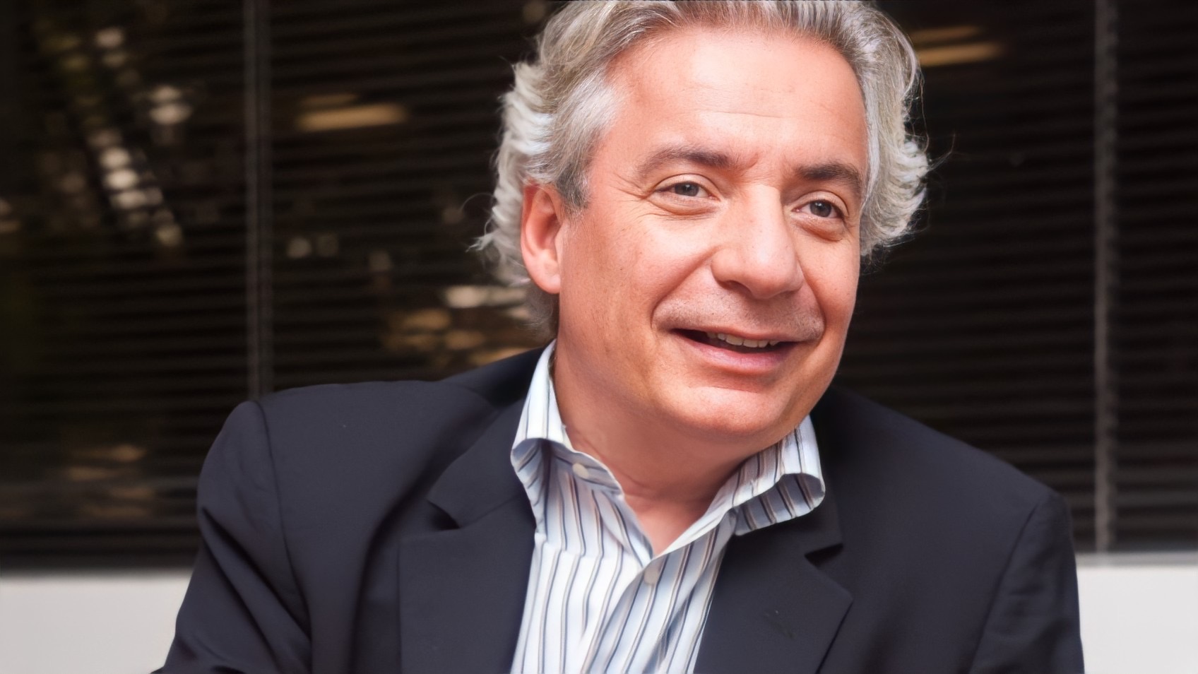 Homem sorridente com cabelos grisalhos e terno azul