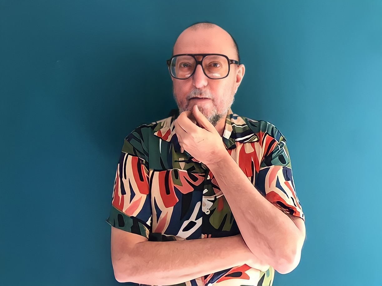 Homem pensativo com óculos e camisa colorida em fundo azul.