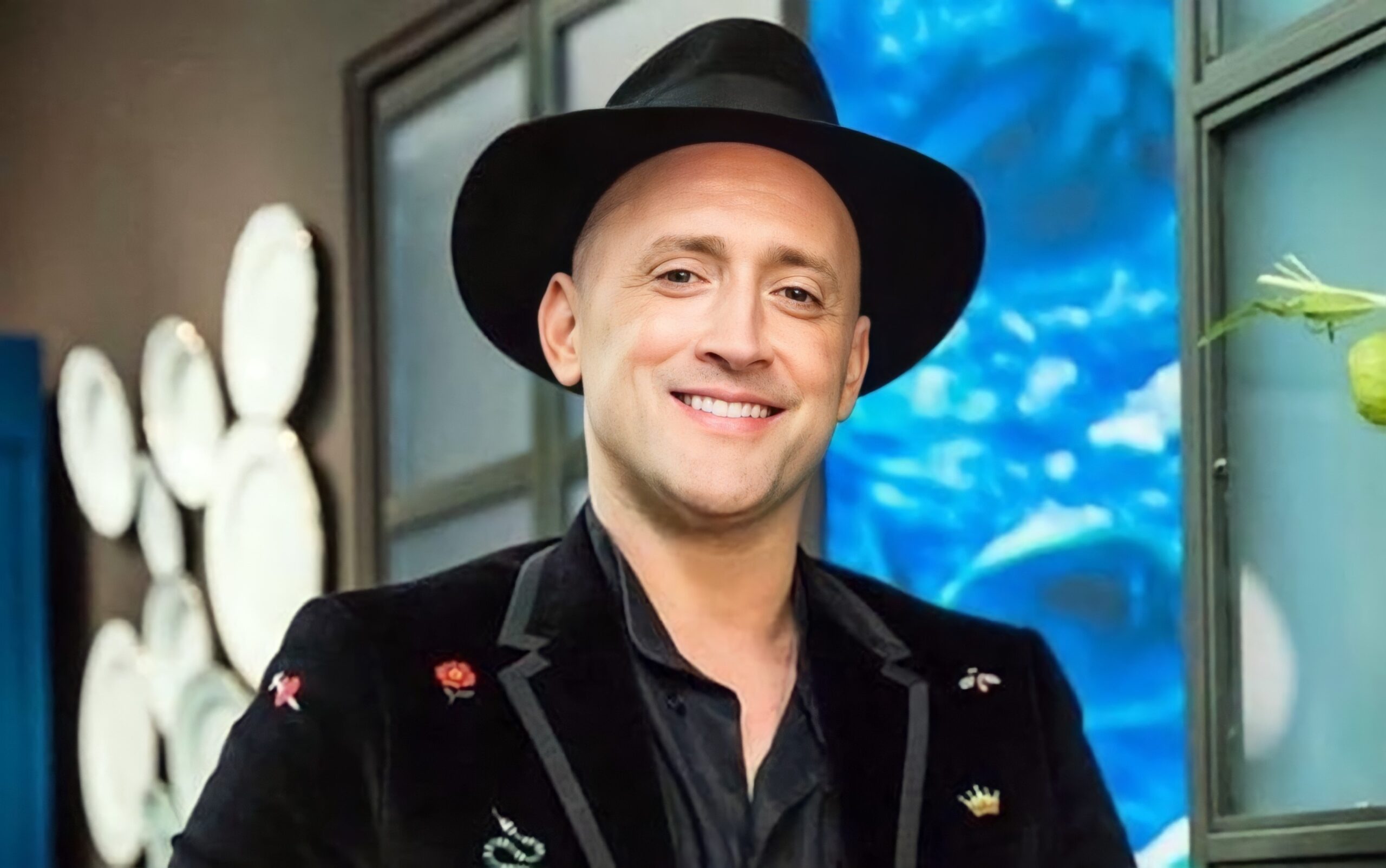 Homem sorridente de chapéu e blazer com broches