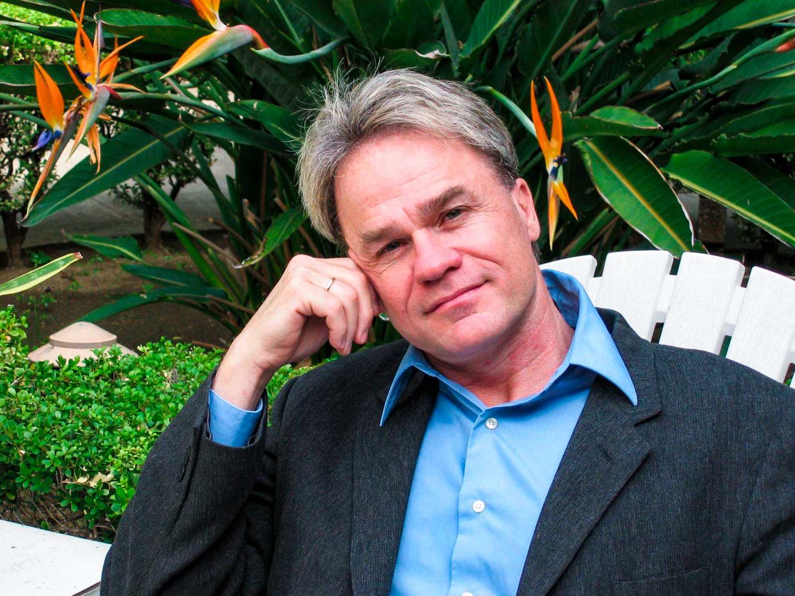 Homem reflexivo em jardim tropical com flores aves-do-paraíso