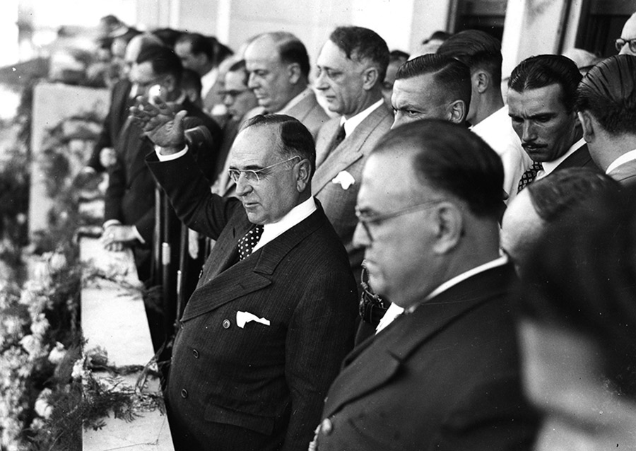 Harry S. Truman acena em evento político formal.