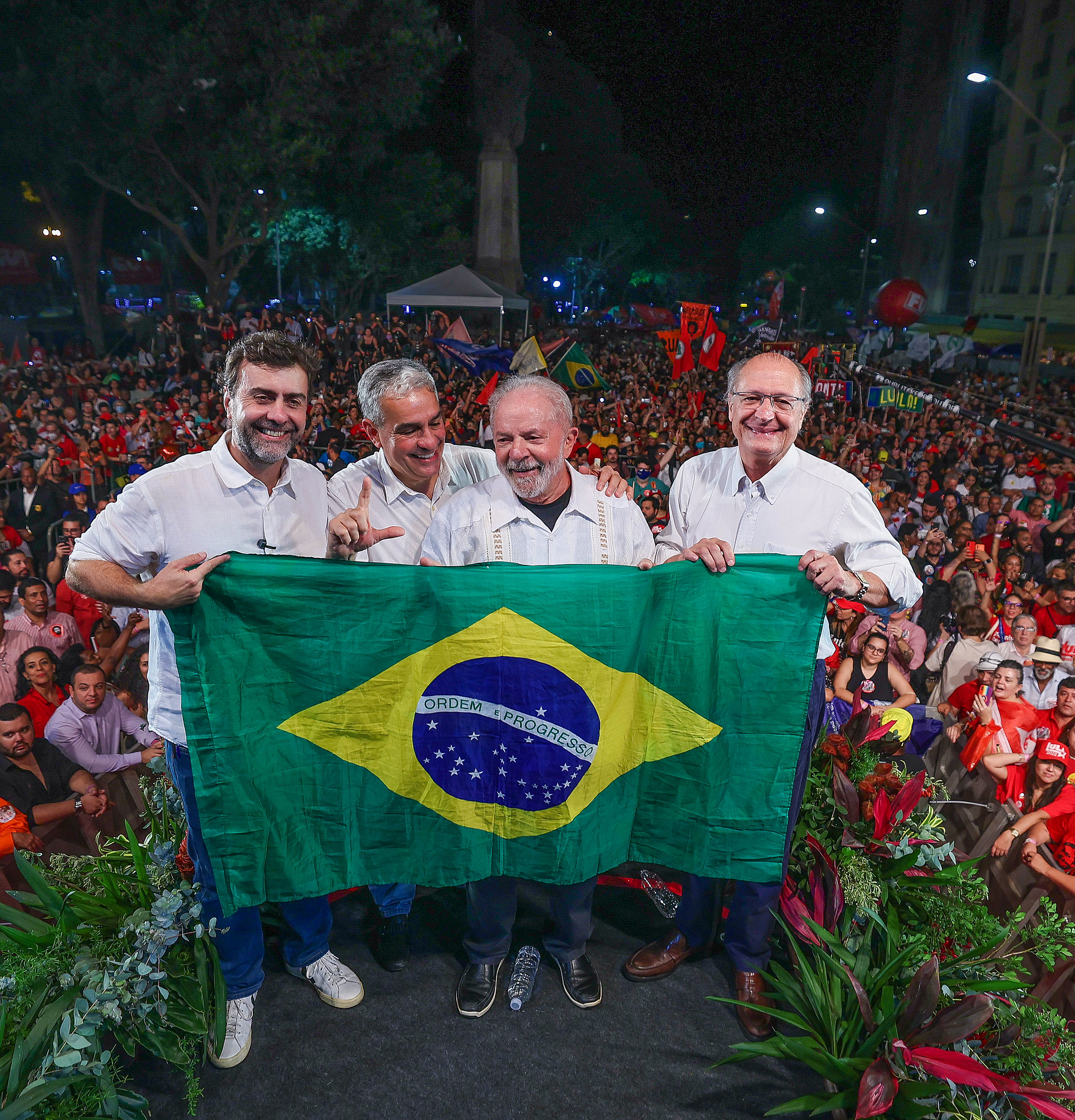 Quatro líderes políticos com a bandeira do Brasil em comício