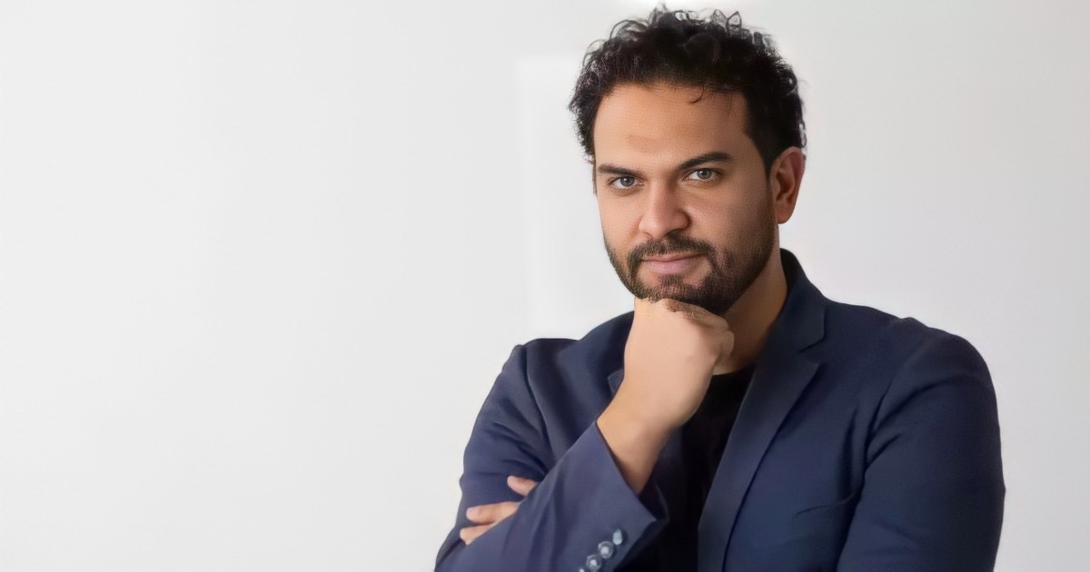 Homem pensativo com blazer azul, olhar direto e confiante.