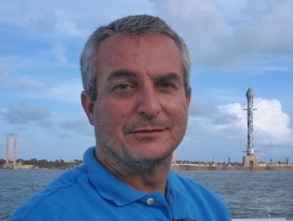 Homem em camisa azul, mar e monumento costeiro.