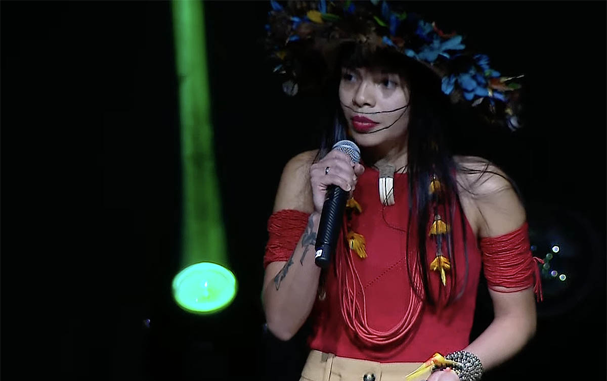 Mulher Indígena Brasileira com Cocar e Microfone no Palco