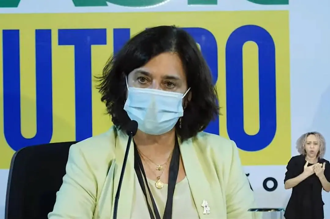 Mulher de máscara em coletiva de imprensa com intérprete de Libras