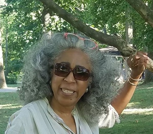 Mulher negra sorrindo, cabelos grisalhos, em parque.