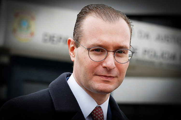 Retrato formal de homem com óculos em ambiente institucional.