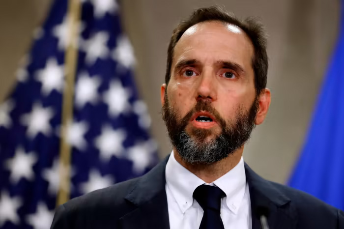 Homem barbudo em coletiva de imprensa com bandeiras ao fundo