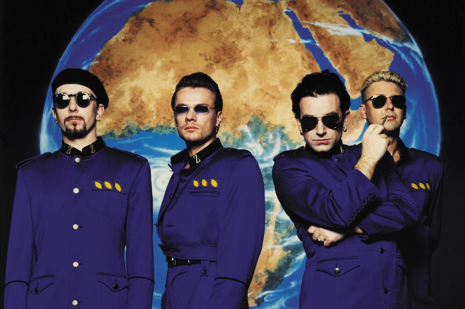 Banda U2 em uniformes futuristas diante do mapa-múndi