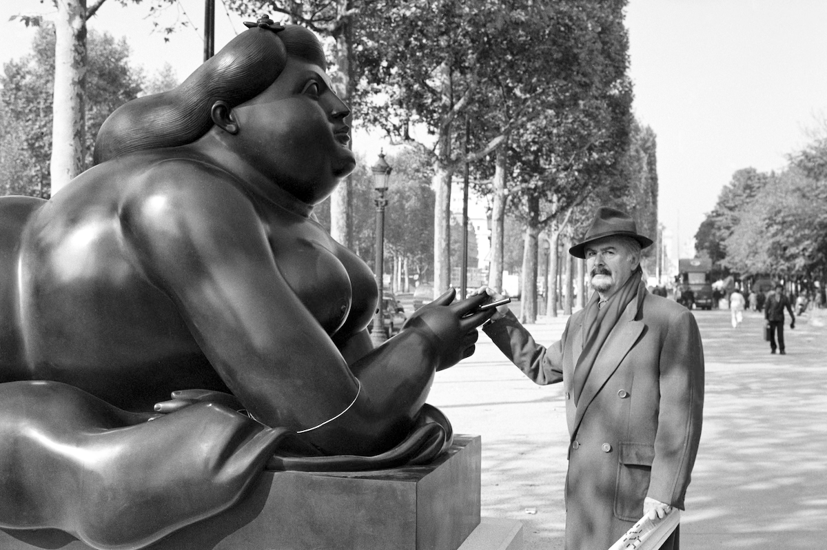Homem interage com escultura de Botero em avenida.