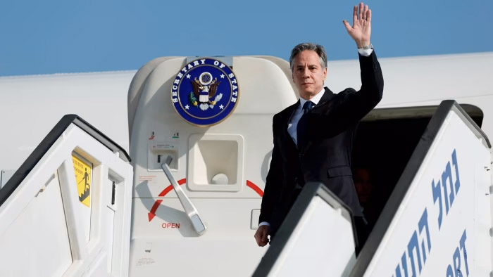 Antony Blinken em visita oficial, acenando em escada de avião.