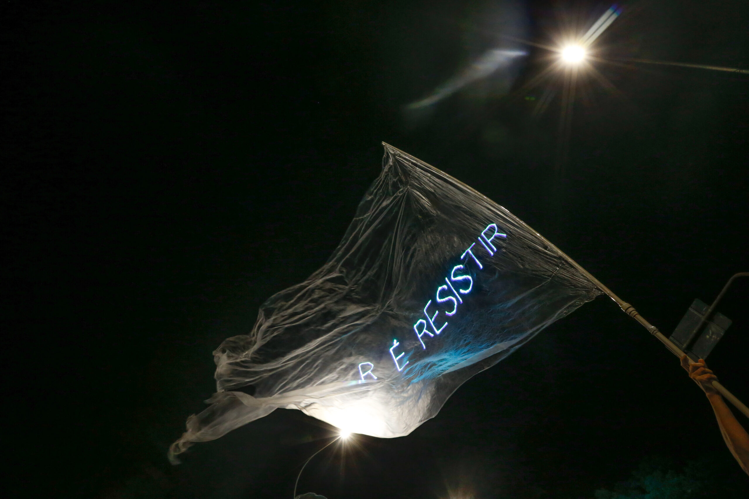 Bandeira translúcida "É Resistir" em protesto noturno