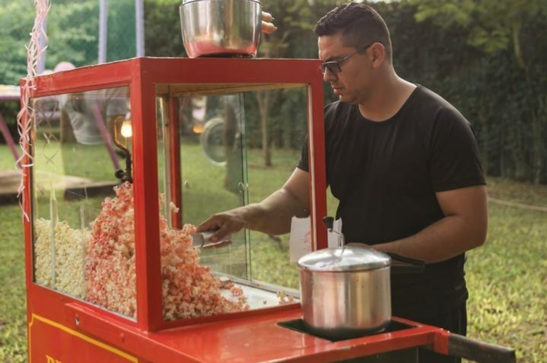 Homem serve pipoca colorida em evento ao ar livre