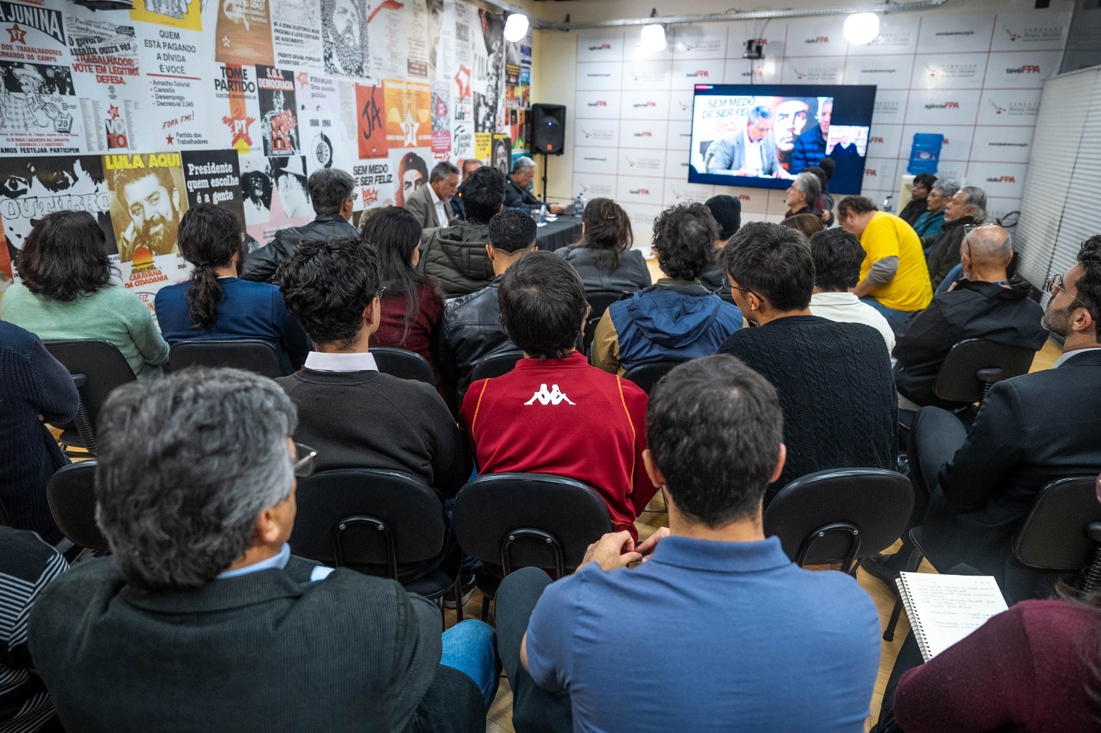 Debate político em sala com cartazes históricos do PT