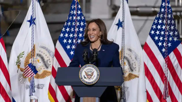 Kamala Harris discursa com bandeiras americanas ao fundo.