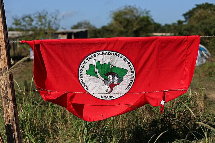 Bandeira do MST em cenário rural simbolizando luta pela terra