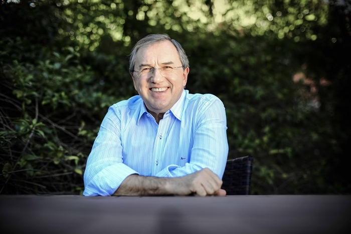 Homem sorridente com óculos e camisa azul, fundo verde